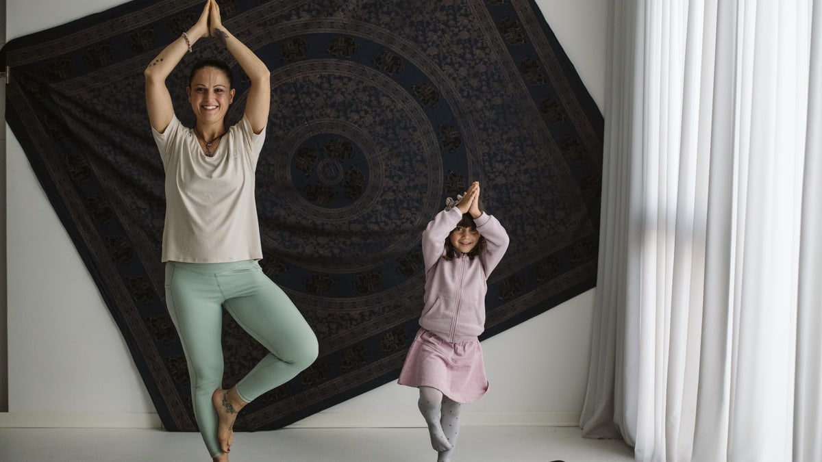 A mom and her daughter perform yoga poses in a cozy home setting, fostering fitness and bonding.